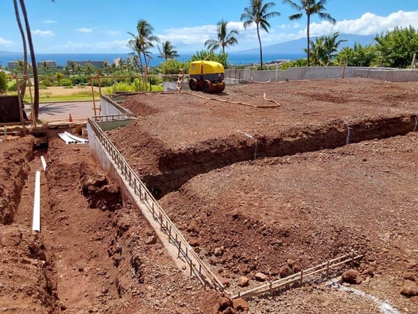 Yellow soil compactor on a recently graded lot, compacting the soil prior to laying the foundation.