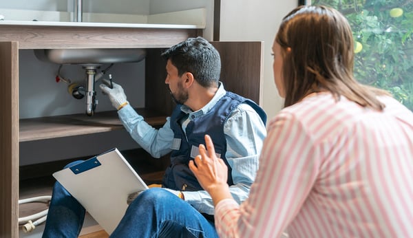 Plumber-explaining-to-a-client-the-problem-with-her-kitchen-sink-1-1