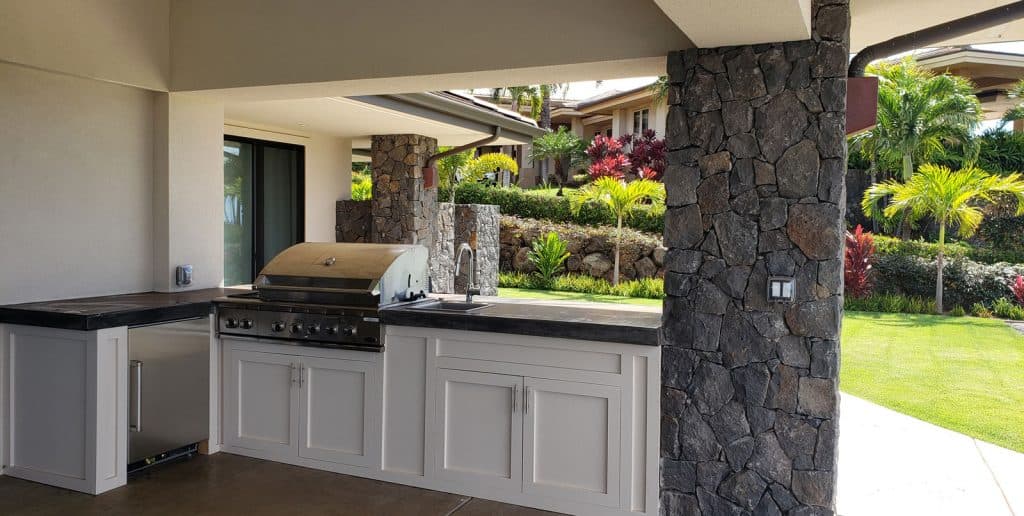 Outdoor kitchen under lanai roof with refrigerator, grill, sink, and plenty of countertop space.